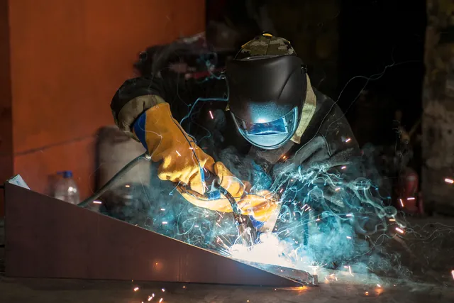 A welder joining a steel section, sparks falling across the bench.